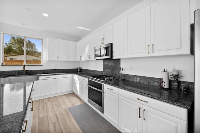 kitchen with dark stone counters, appliances with stainless steel finishes, light wood-style floors, white cabinetry, and a sink