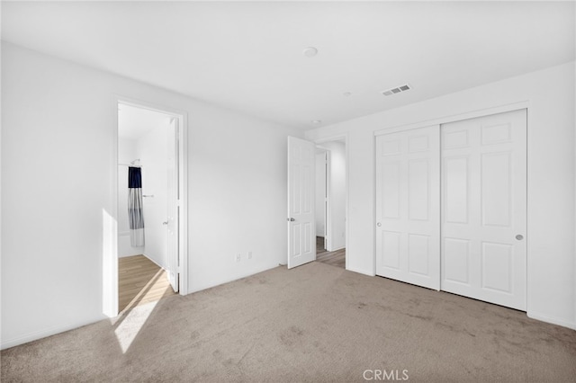 unfurnished bedroom featuring visible vents, a closet, ensuite bath, and carpet flooring