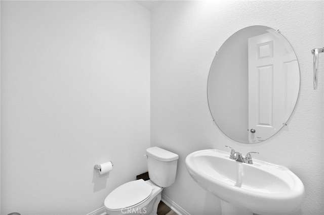 half bathroom with toilet, baseboards, and a sink