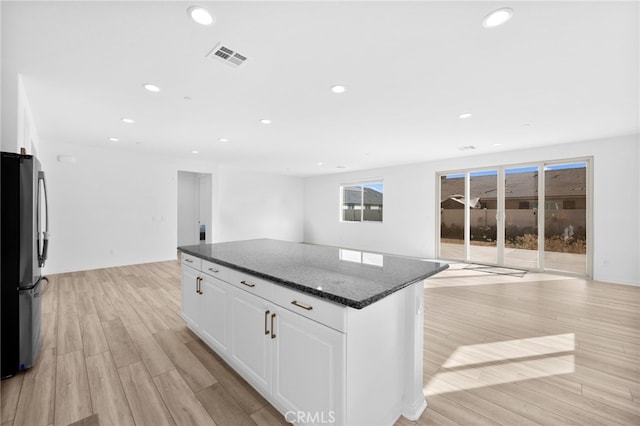 kitchen featuring a kitchen island, open floor plan, dark stone counters, light wood-style flooring, and freestanding refrigerator