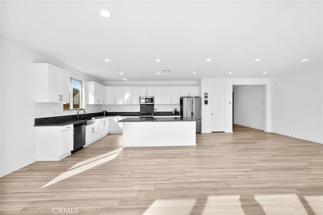 kitchen featuring a kitchen island, dark countertops, stainless steel appliances, light wood-style floors, and white cabinets