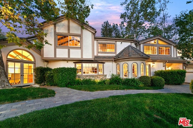 back house at dusk featuring a lawn and french doors