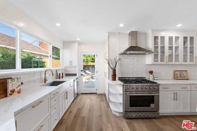 kitchen with white cabinets, appliances with stainless steel finishes, wall chimney range hood, and sink