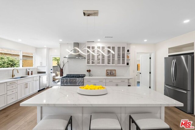 kitchen with a kitchen breakfast bar, appliances with stainless steel finishes, sink, wall chimney range hood, and decorative light fixtures