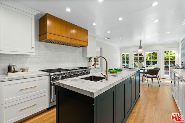 kitchen featuring stainless steel range, white cabinets, custom range hood, and an island with sink