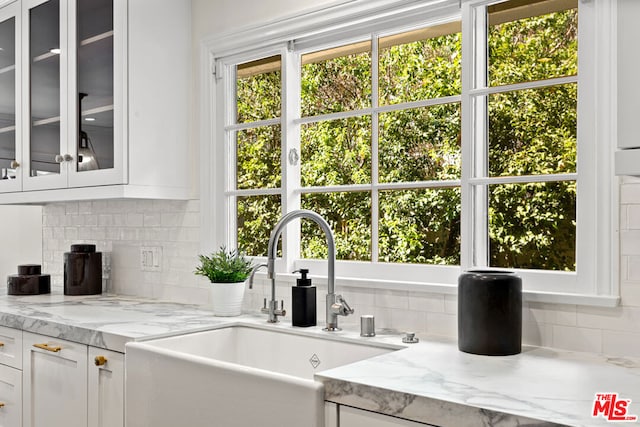 kitchen featuring white cabinets, backsplash, light stone countertops, and sink