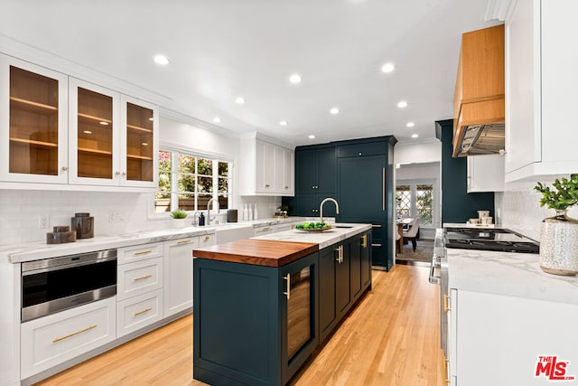 kitchen featuring white cabinetry, butcher block countertops, a kitchen island with sink, ornamental molding, and sink