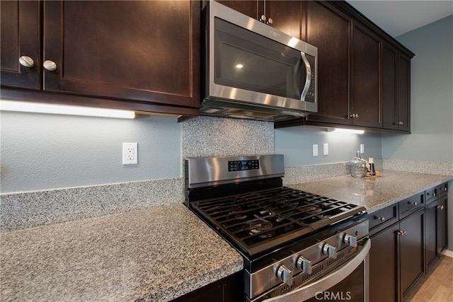 kitchen featuring stainless steel appliances, dark brown cabinets, and light stone counters