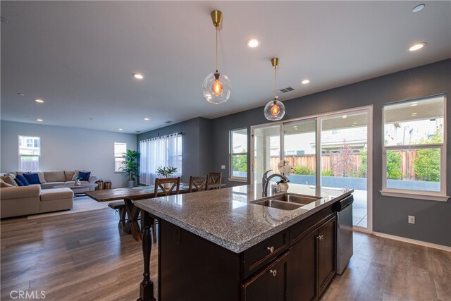 kitchen with pendant lighting, sink, light stone counters, a center island with sink, and stainless steel dishwasher