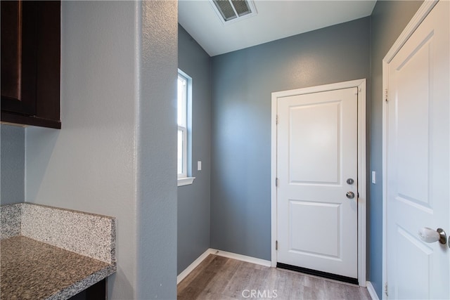 doorway with light wood finished floors, baseboards, and visible vents