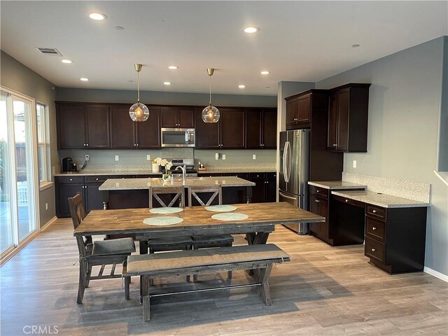 kitchen featuring hanging light fixtures, stainless steel appliances, dark brown cabinetry, light hardwood / wood-style floors, and light stone countertops