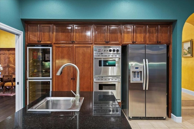 kitchen with sink, light tile patterned floors, appliances with stainless steel finishes, dark stone countertops, and beverage cooler