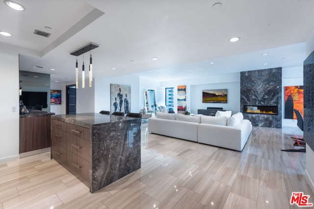 kitchen featuring pendant lighting, dark stone counters, a center island, dark brown cabinetry, and a premium fireplace