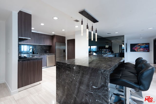 kitchen with a breakfast bar, hanging light fixtures, dark brown cabinets, stainless steel appliances, and backsplash