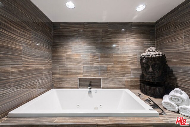 bathroom with a relaxing tiled tub and tile walls