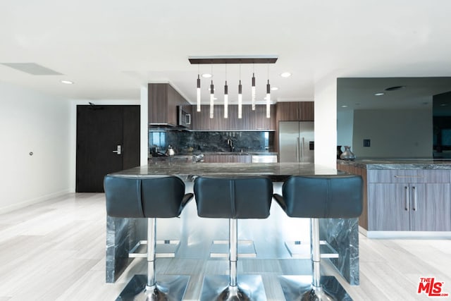 kitchen with a breakfast bar, hanging light fixtures, stainless steel appliances, dark brown cabinetry, and decorative backsplash