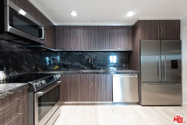 kitchen with appliances with stainless steel finishes, sink, decorative backsplash, dark stone counters, and dark brown cabinets