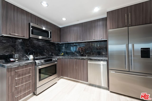 kitchen with dark brown cabinetry, sink, tasteful backsplash, appliances with stainless steel finishes, and dark stone counters