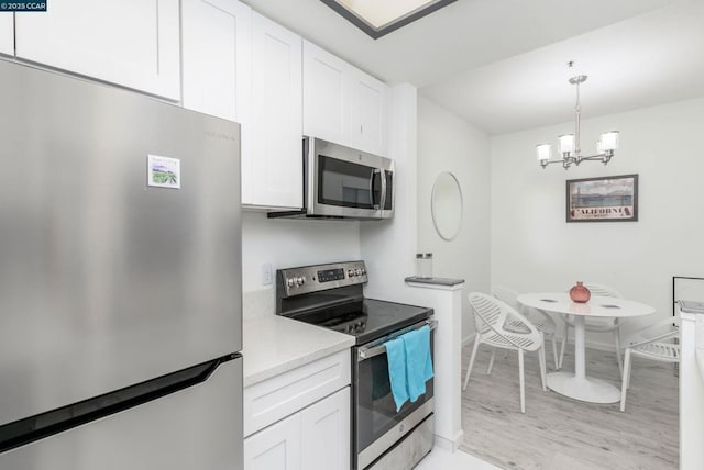 kitchen featuring light wood-type flooring, an inviting chandelier, stainless steel appliances, and white cabinetry