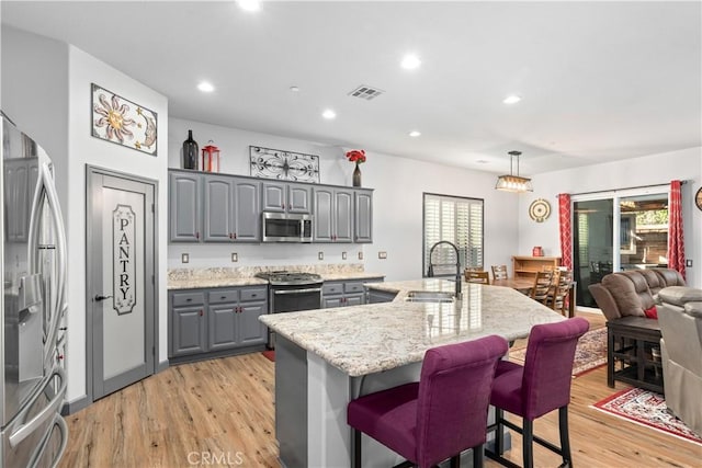 kitchen featuring an island with sink, stainless steel appliances, gray cabinetry, pendant lighting, and sink