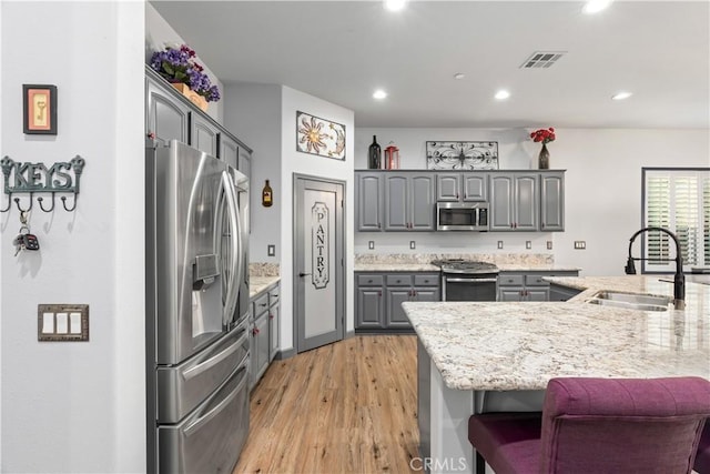 kitchen with light stone countertops, stainless steel appliances, light hardwood / wood-style floors, sink, and gray cabinetry