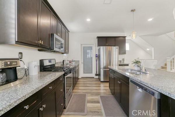 kitchen featuring pendant lighting, sink, light stone countertops, stainless steel appliances, and dark brown cabinets