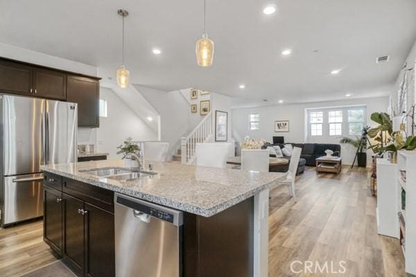 kitchen featuring stainless steel appliances, a kitchen island with sink, dark brown cabinets, hanging light fixtures, and sink