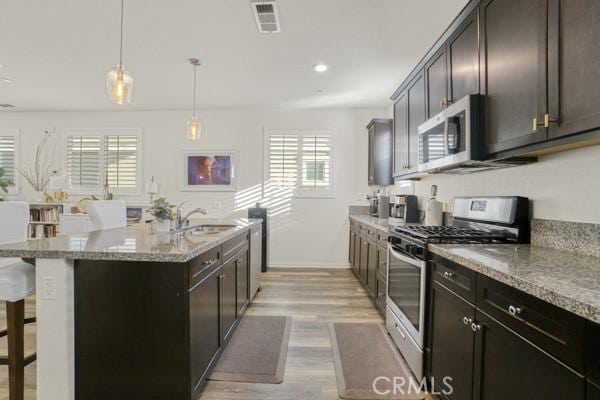 kitchen with a center island with sink, appliances with stainless steel finishes, decorative light fixtures, a breakfast bar, and sink