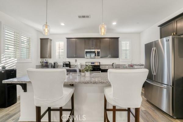 kitchen with a breakfast bar, a center island with sink, appliances with stainless steel finishes, pendant lighting, and dark brown cabinetry