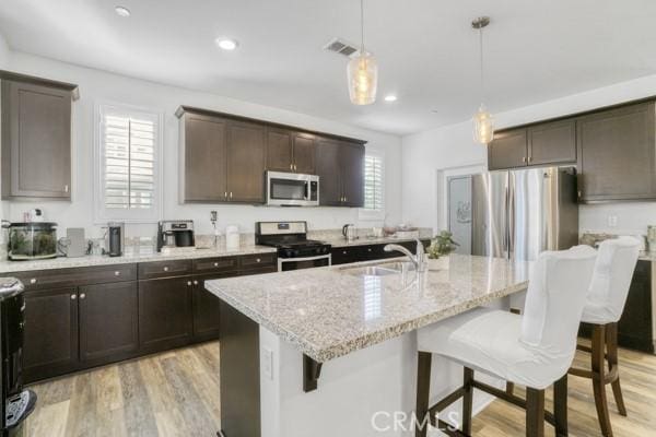 kitchen with light hardwood / wood-style floors, an island with sink, stainless steel appliances, pendant lighting, and sink