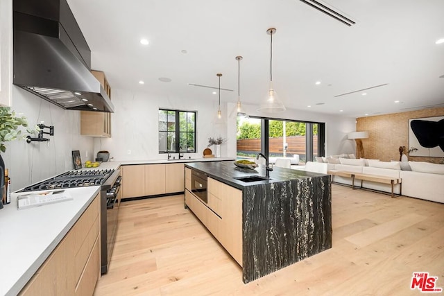 kitchen with range with gas cooktop, wall chimney exhaust hood, light brown cabinets, an island with sink, and sink