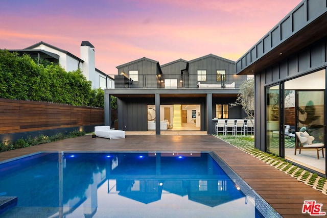 pool at dusk with a wooden deck and exterior bar