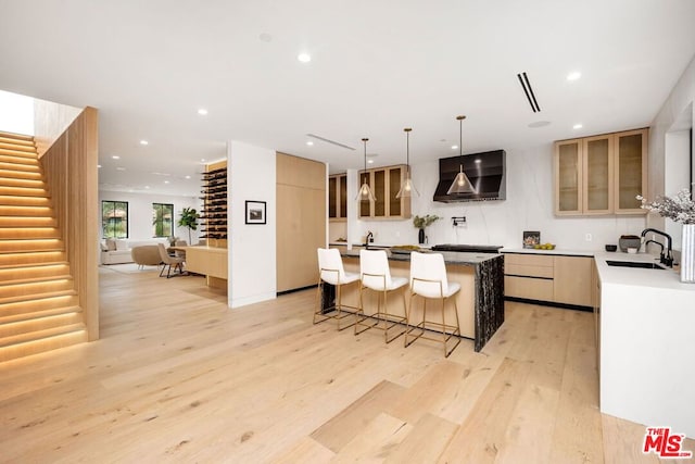 kitchen featuring wall chimney range hood, a center island, sink, light wood-type flooring, and a breakfast bar area