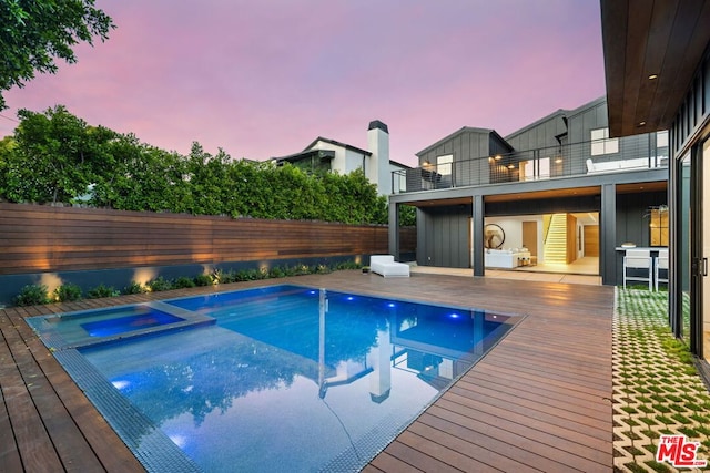 pool at dusk featuring a wooden deck and an in ground hot tub