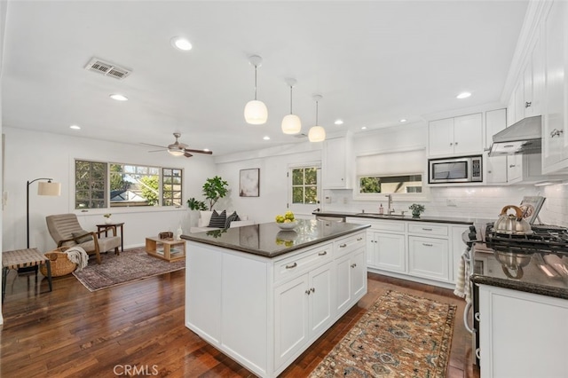 kitchen featuring stainless steel microwave, decorative light fixtures, white cabinets, and a kitchen island