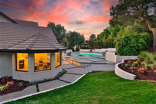 pool at dusk with a patio area and a yard