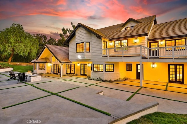 back house at dusk featuring an outdoor fire pit, a balcony, and a patio