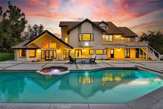 back house at dusk featuring a pool with hot tub and a patio area