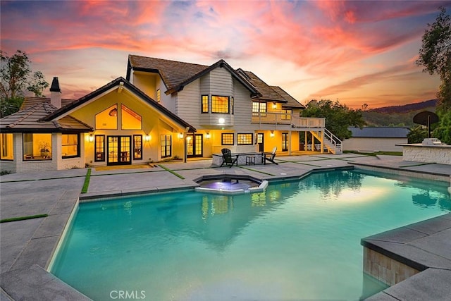 pool at dusk with an in ground hot tub and a patio area