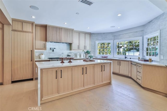 kitchen with stainless steel gas stovetop, sink, light hardwood / wood-style flooring, a kitchen island with sink, and light brown cabinetry