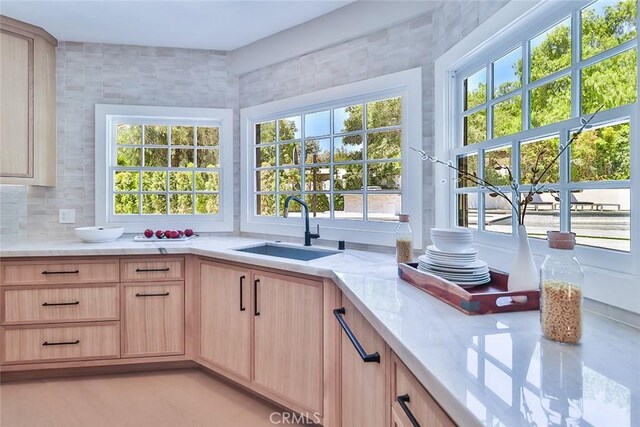 kitchen featuring backsplash, light stone counters, sink, and light brown cabinets