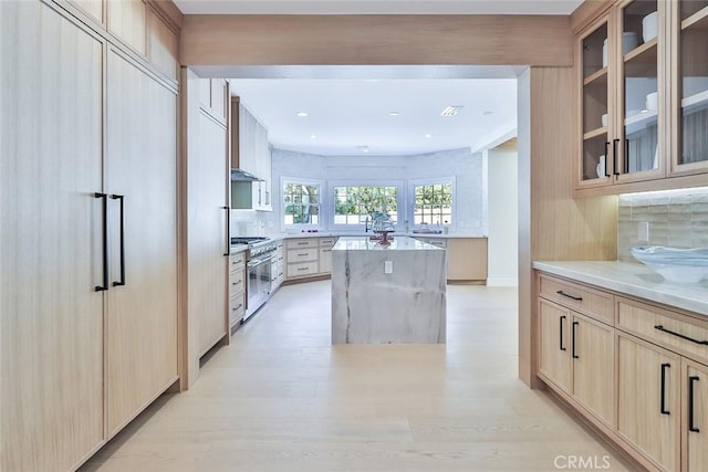 kitchen with a kitchen island, decorative backsplash, light stone countertops, light brown cabinetry, and high quality appliances