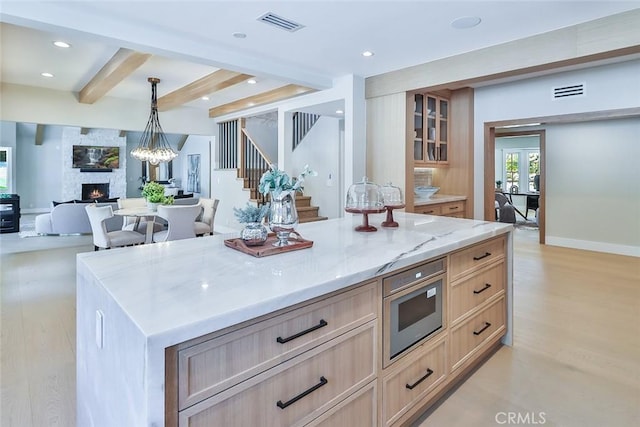 kitchen featuring a fireplace, pendant lighting, beamed ceiling, light brown cabinets, and a large island