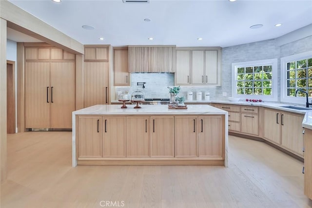 kitchen featuring light brown cabinets, tasteful backsplash, an island with sink, sink, and light hardwood / wood-style flooring