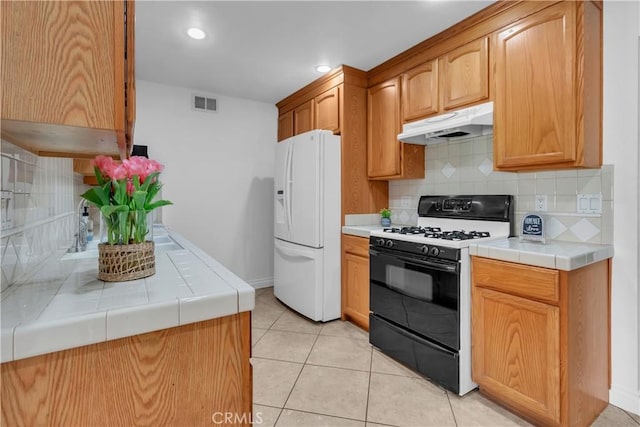 kitchen featuring under cabinet range hood, visible vents, tile counters, white fridge with ice dispenser, and gas range