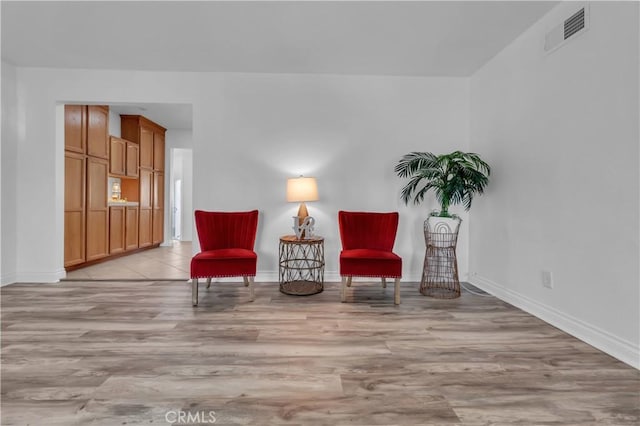 sitting room featuring light wood-style flooring, visible vents, and baseboards