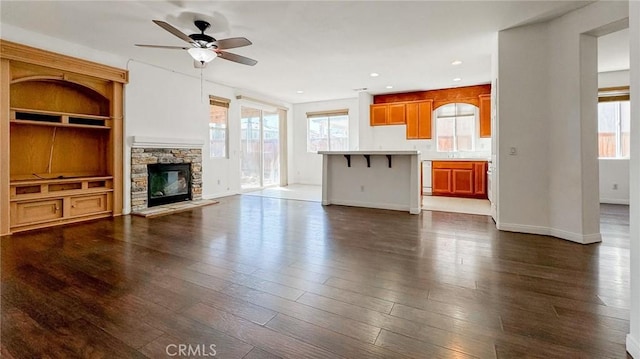 unfurnished living room featuring ceiling fan, dark hardwood / wood-style floors, and a stone fireplace