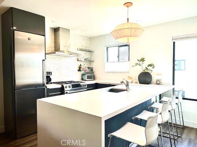 kitchen featuring appliances with stainless steel finishes, dark wood-type flooring, wall chimney range hood, sink, and a breakfast bar