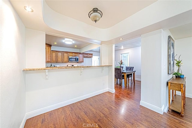 kitchen featuring a kitchen bar, light stone counters, dark hardwood / wood-style floors, and kitchen peninsula