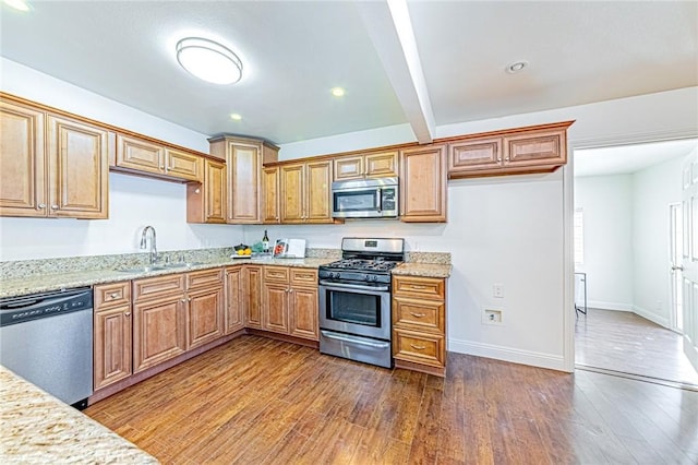 kitchen with dark wood-type flooring, stainless steel appliances, light stone counters, and sink